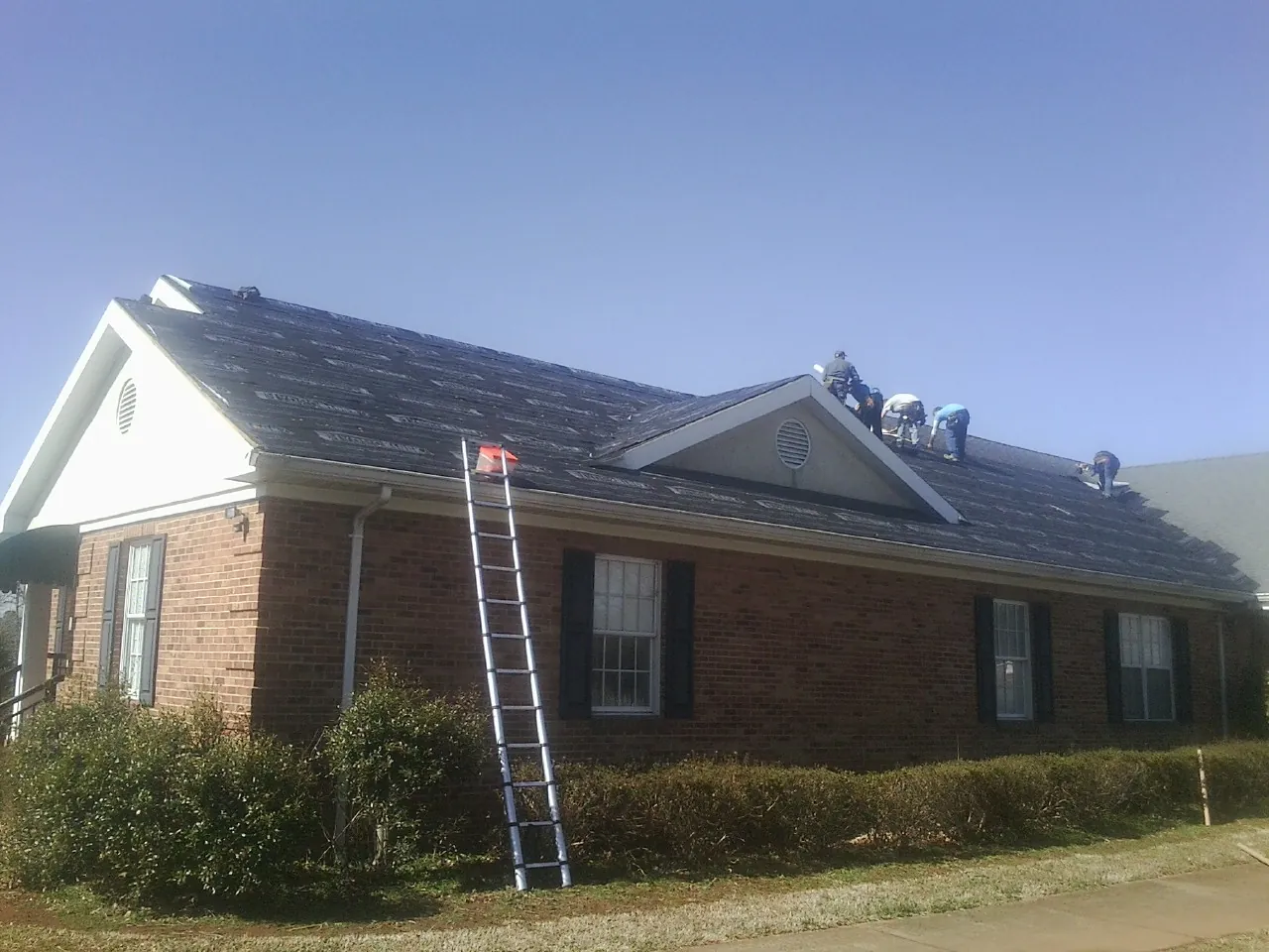 Crew tearing shingles off a brick ranch roof with a ladder set — Emergency Roof Repair work by our crew in Reelsville