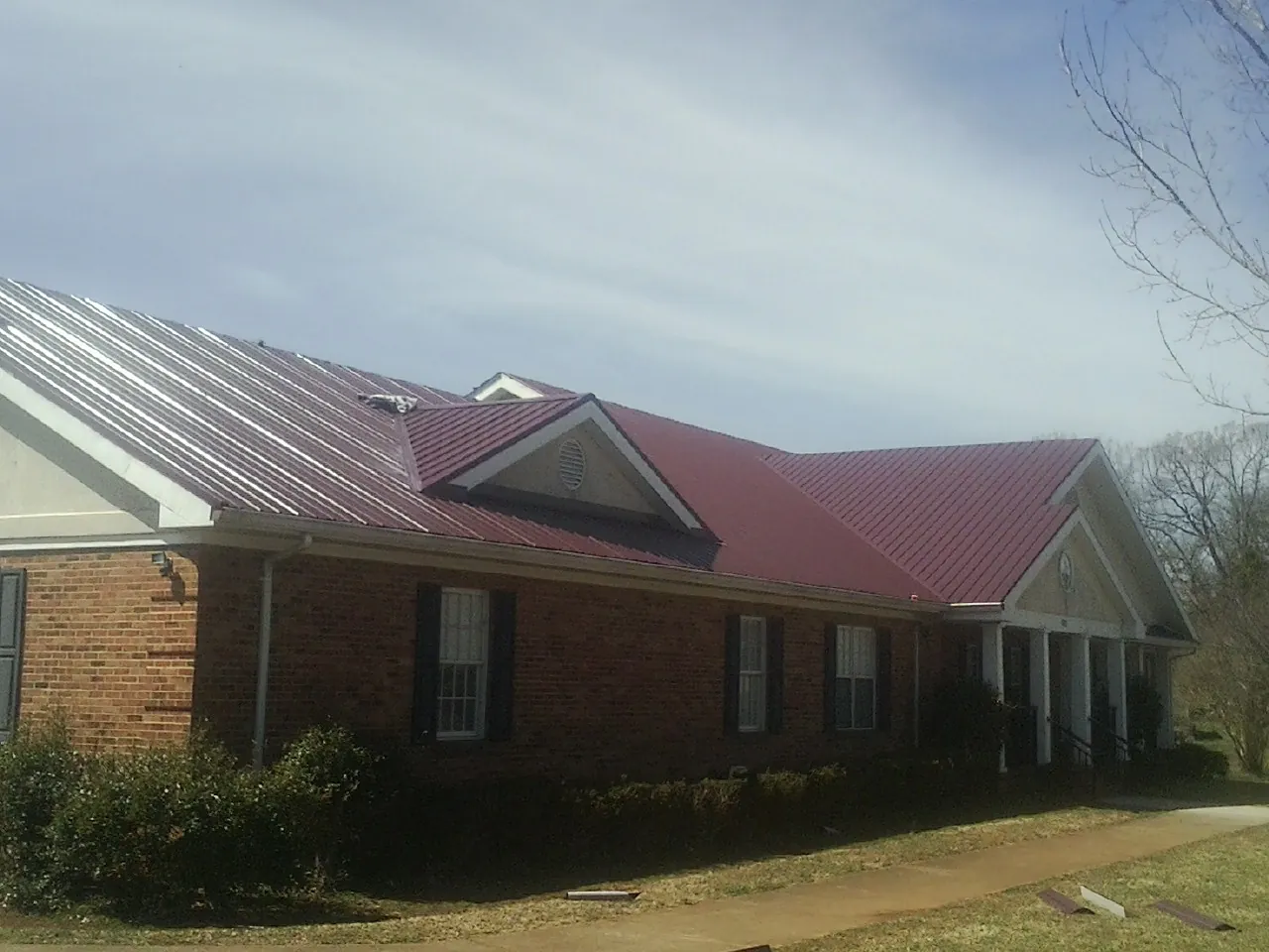 Red metal roof with gabled entries on a long brick building, from a Hail Damage Roof Repair job in Reelsville