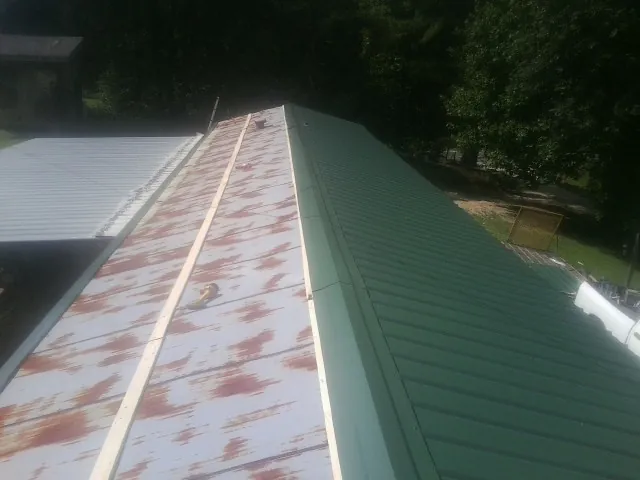 Old rusted panels beside newly installed green metal roofing — Wind Damage Roof Repair by Roofing Brothers in Reelsville