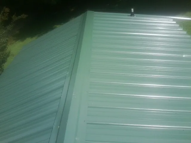 New green metal panels meeting at the ridge of a roof — Flat Roof Repair work by our crew in Reelsville