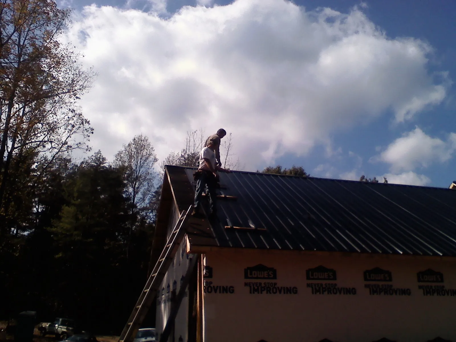 Roofer fastening dark metal panels high against a cloudy sky, from a Roof Inspection job in Reelsville