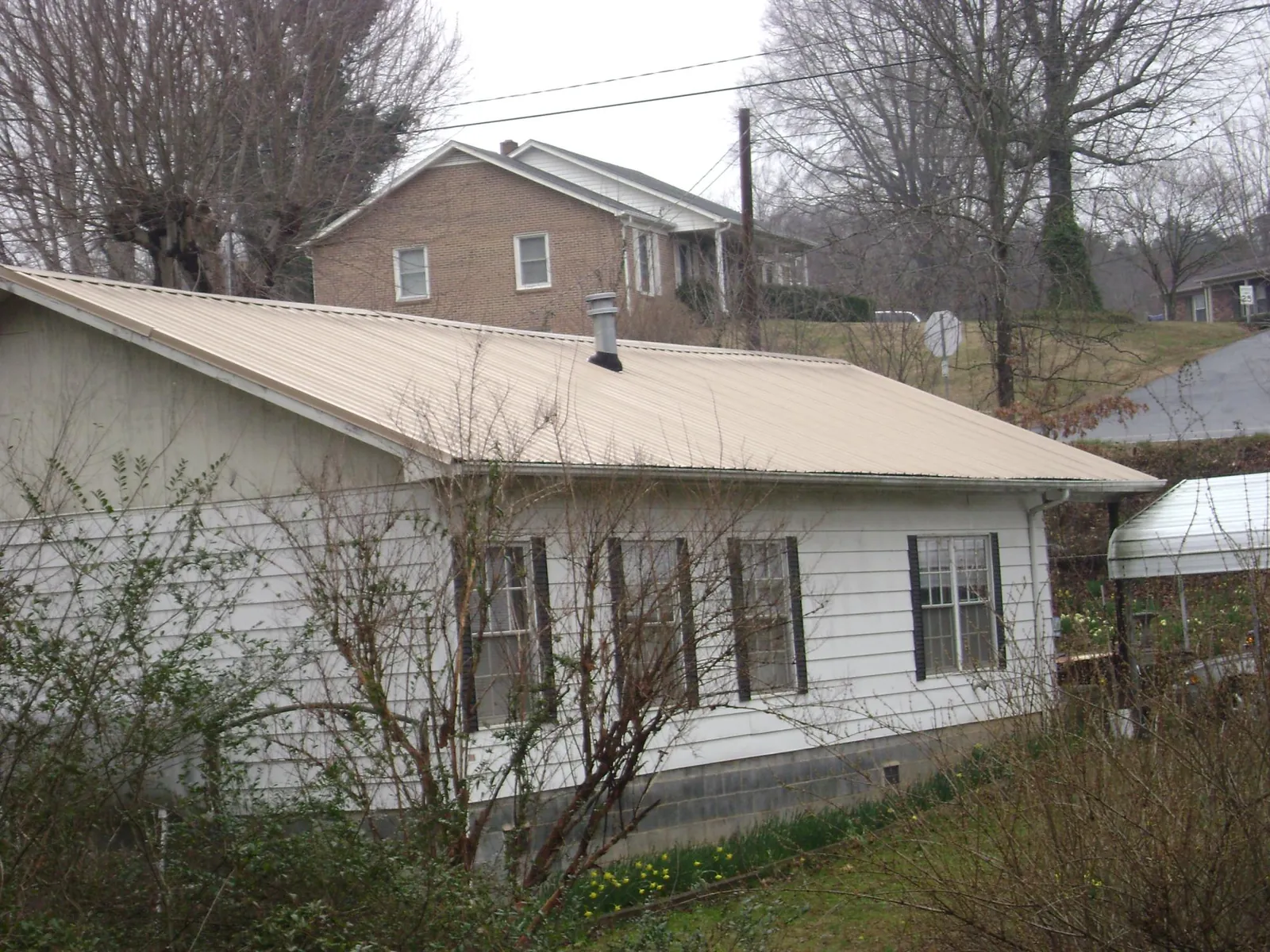 Tan metal roof on a white sided house set into a hillside — Commercial Roofing by Roofing Brothers in Reelsville